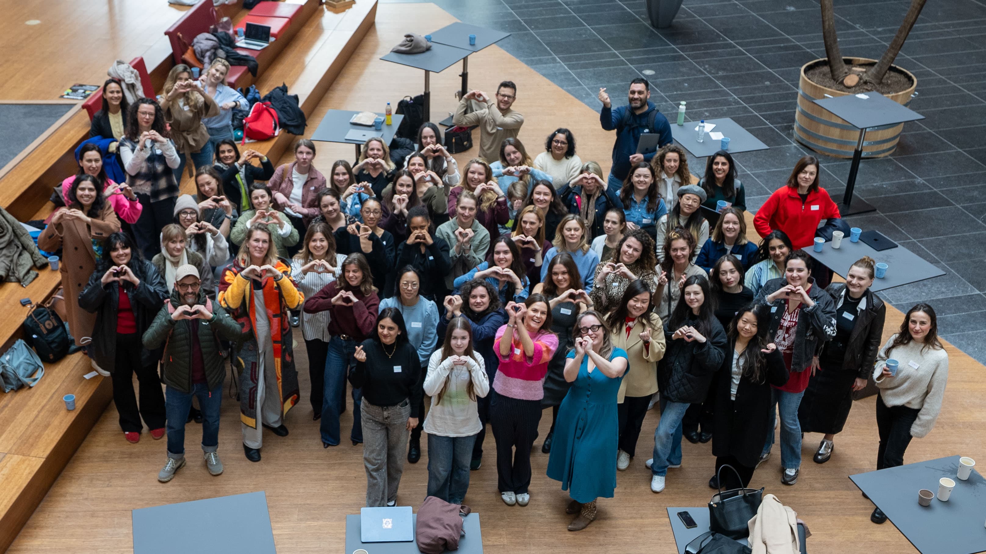 Aerial view of a Ladies Build With AI group photo, dozens of women and a few men making heart shapes with their hands in an atrium